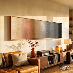 May include: A long, rectangular wall art piece featuring a textured gradient of colours transitioning from light beige and soft pink to muted grey, green, and deep black, enclosed in a thin wooden frame and mounted horizontally on a wall.
