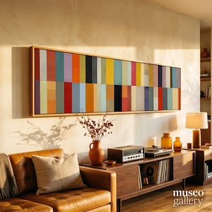 Può includere: Un'opera d'arte da parete lunga e rettangolare caratterizzata da una griglia di pannelli verticali multicolori nelle tonalità del rosso, arancione, giallo, blu, viola e nero, incorniciata in legno chiaro. L'opera è esposta sopra un mobile multimediale.