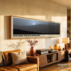 Pode incluir: Uma impressão artística panorâmica emoldurada intitulada BLUE SUNSET OVER GALE CRATER, MARS. A imagem mostra uma paisagem escura e silhuetada sob um sol pálido. O texto abaixo da imagem explica que a poeira em suspensão dispersa a luz vermelha.