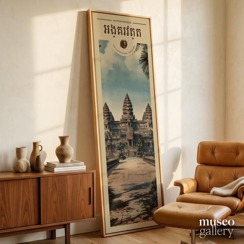 Pu&ograve; includere: Un'alta opera d'arte da parete incorniciata di forma rettangolare che presenta un'illustrazione dettagliata del complesso del tempio di Angkor Wat. La stampa include caratteri khmer nella parte superiore e un emblema circolare. L'opera &egrave; in una cornice di legno chiaro.