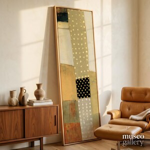 May include: A tall, rectangular framed abstract painting featuring vertical panels of muted earth tones, including beige, tan, and olive green, accented by a central column of white and black polka dots, all enclosed within a light wood frame.