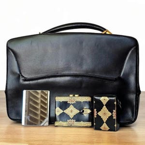 Cartera con asa superior de cuero negro Rosenfeld de los años 50 y 60 con detalles y herrajes de latón, MÁS una billetera a juego, una caja de cigarrillos y un espejo