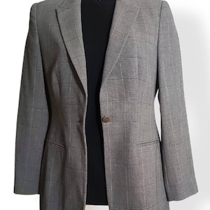 May include: A gray blazer with a plaid pattern. The blazer has a single-button closure and a notched lapel. The blazer is displayed on a mannequin with a black top underneath.