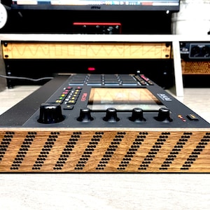 Könnte beinhalten: Eine schwarze Musikproduktions-Workstation mit einer Holzseitenteil mit einem Chevron-Muster. Das Gerät verfügt über einen Bildschirm, Knöpfe und Tasten.