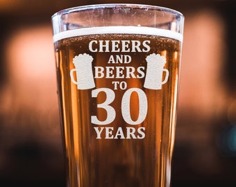 May include: A clear glass pint glass with a brown beer inside. The glass has the text "Cheers and Beers to 30 Years" etched on the side.