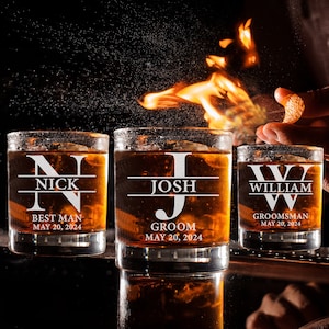 May include: Three personalized whiskey glasses with the names "Nick", "Josh", and "William" etched on them. The glasses are filled with amber liquid and have the words "Best Man", "Groom", and "Groomsman" printed below the names. The date "May 20, 2024" is printed below each title.