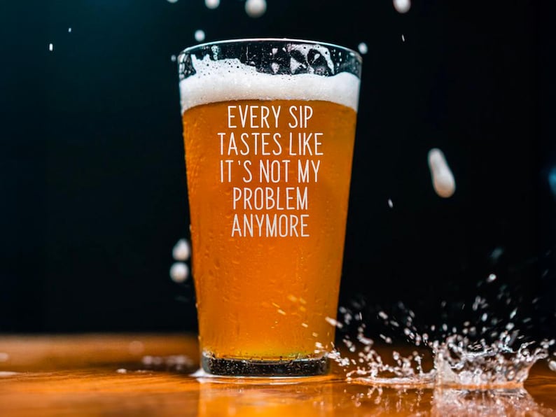 Pode incluir: Um copo de cerveja &acirc;mbar com uma espuma branca. O copo tem condensa&ccedil;&atilde;o e o texto branco "EVERY SIP TASTES LIKE IT'S NOT MY PROBLEM ANYMORE". Gotas e salpicos de &aacute;gua rodeiam o copo.