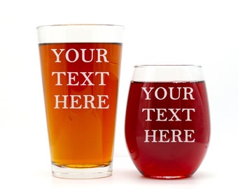 Puede incluir: Dos vasos para beber de vidrio transparente con el texto "YOUR TEXT HERE" grabado en ellos. El vaso de la izquierda es un vaso de pinta lleno de un líquido marrón. El vaso de la derecha es una copa de vino llena de un líquido rojo.