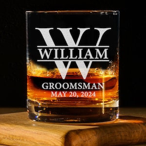 May include: A clear glass with a personalized inscription. The inscription reads "W WILLIAM GROOMSMAN MAY 20, 2024". The glass is filled with a brown liquid.