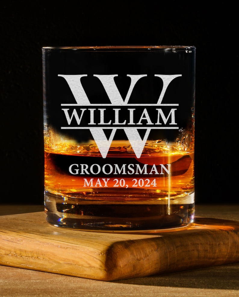 May include: A clear glass with a personalized inscription. The inscription reads "W WILLIAM GROOMSMAN MAY 20, 2024". The glass is filled with a brown liquid.