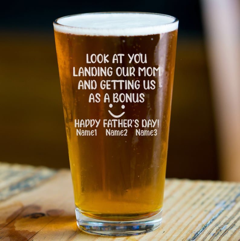 May include: A clear glass beer stein with a humorous message that reads "Look at you landing our mom and getting us as a bonus. Happy Father's Day!" The message is etched into the glass. The stein is filled with a golden-colored beer.