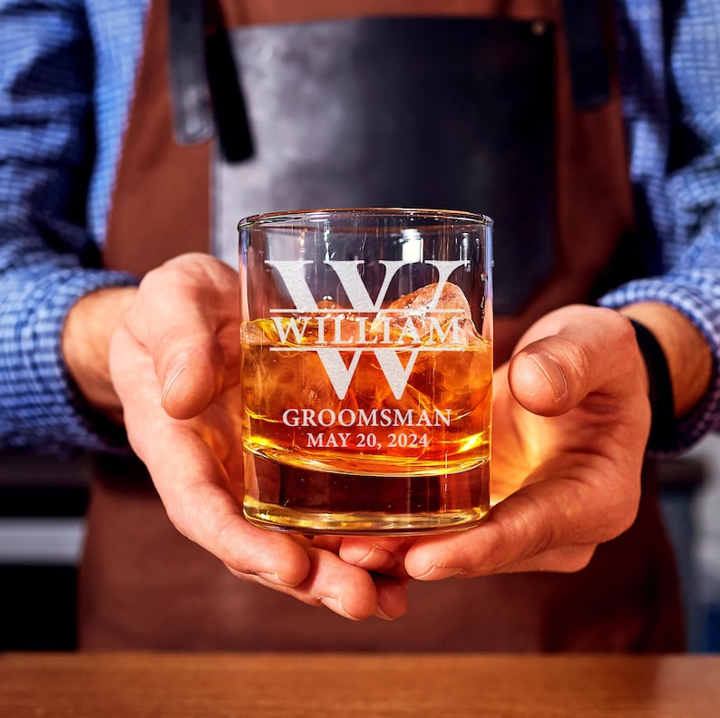May include: A clear glass whiskey tumbler with the name "William" etched on the front. The glass also has the words "Groomsman" and "May 20, 2024" etched on it.