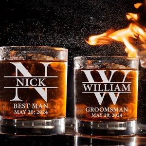 May include: Two personalized whiskey glasses with the names "Nick" and "William" etched on them. The glasses are filled with amber liquid and have the words "Best Man" and "Groomsman" along with the date "May 20, 2024" printed on them.