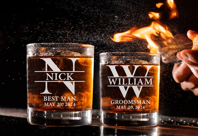 May include: Two personalized whiskey glasses with the names "Nick" and "William" etched on them. The glasses are filled with amber liquid and have the words "Best Man" and "Groomsman" along with the date "May 20, 2024" printed on them.