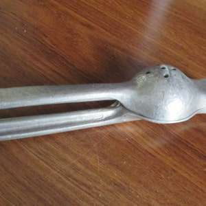 May include: A silver metal citrus juicer with a handle and a textured surface. The juicer is designed to squeeze lemons, limes, and oranges.