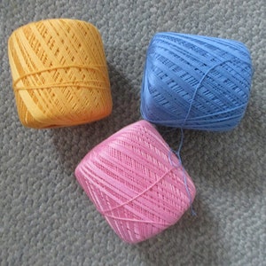 May include: Three balls of yarn in different colors: orange, light blue, and pink. The yarn is wound into balls and has a striped pattern.