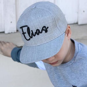 Könnte beinhalten: Eine graue und schwarze Baseballkappe mit dem Namen "Elias" in schwarzer kursivschrift gestickt.