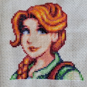 Puede incluir: Bordado de punto de cruz de una mujer con cabello rojo, vistiendo una camisa verde y roja. La mujer sonríe y mira hacia la derecha.