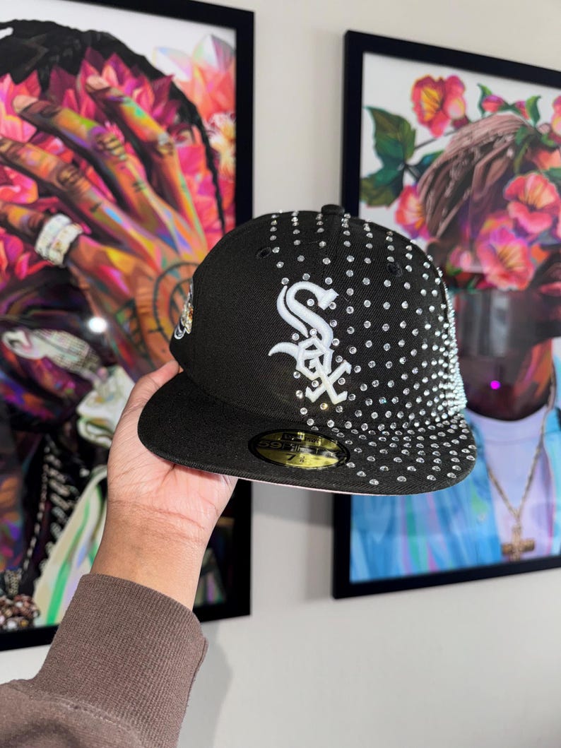 Pode incluir: Um bon&eacute; de beisebol preto com um logotipo 'S' branco e strass. O bon&eacute; tem uma aba preta e uma aba interna branca.