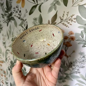 May include: A small, speckled ceramic bowl with a green glaze and the words "sweet treat" written on the inside.