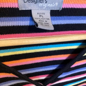 May include: A black, petite, 100% cotton top with horizontal stripes in various colours, including pink, orange, yellow, blue, and purple. The top has a V-neck and a tag that reads "Designers Originals."