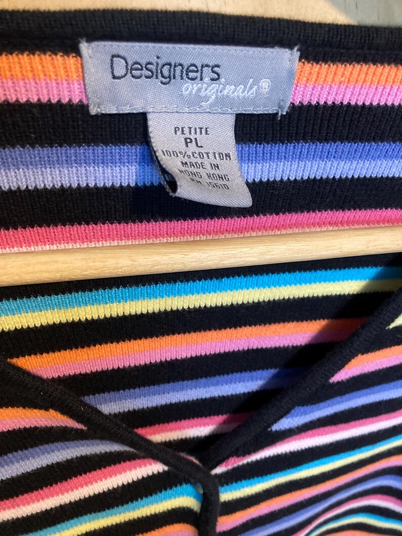 May include: A black, petite, 100% cotton top with horizontal stripes in various colours, including pink, orange, yellow, blue, and purple. The top has a V-neck and a tag that reads "Designers Originals."