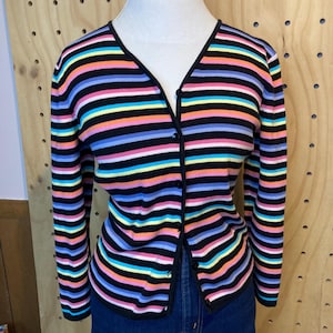 May include: A colourful striped cardigan with a V-neck and long sleeves. The sweater has horizontal stripes in black, pink, orange, yellow, blue, and purple. The cardigan is buttoned up and displayed on a mannequin.