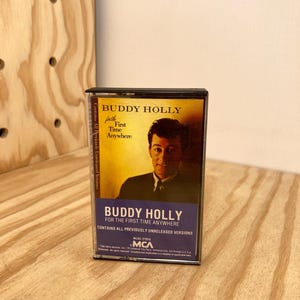 May include: A black cassette tape case with a photo of Buddy Holly on the front. The case has the title "Buddy Holly for the First Time Anywhere" and the text "Contains All Previously Unreleased Versions".