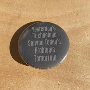 May include: A round, silver button with the text "Yesterday's Technology Solving Today's Problems Tomorrow" engraved on it.