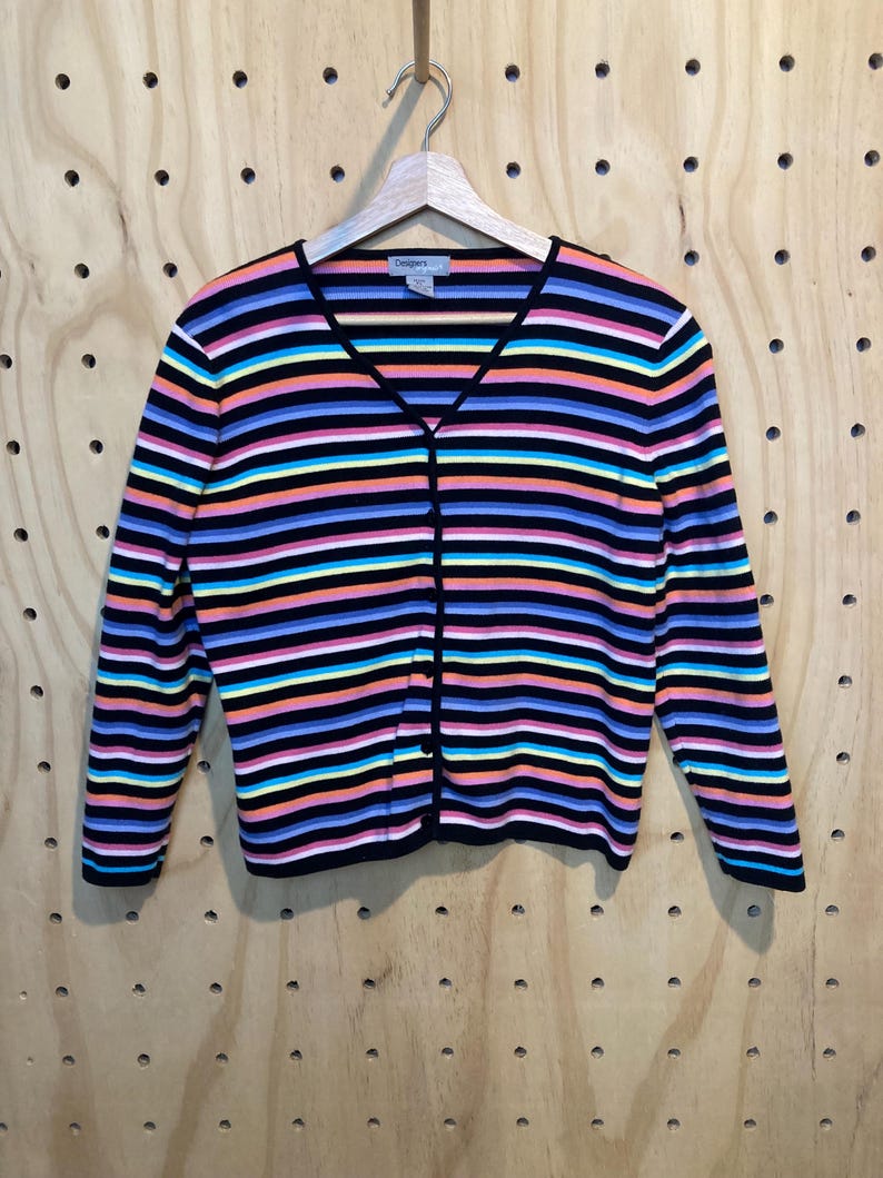 May include: A colourful striped cardigan with a V-neck and button fastening. The sweater has horizontal stripes in black, pink, orange, blue, and yellow. The brand name "Designers" is visible on the label.