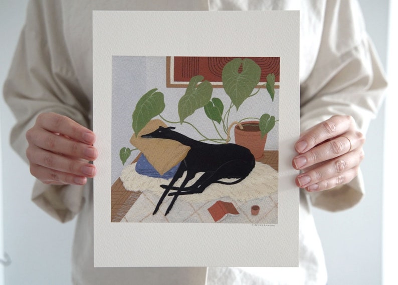 May include: A black and white illustration of a dog sleeping on a rug with a plant in a terracotta pot in the background. The dog is lying on a pillow and there is a book and a cup on the rug.