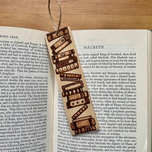 Può includere: Un segnalibro in legno con un design bruciato di libri impilati. Il segnalibro è alto circa 15 cm e largo 4 cm. Il segnalibro è di colore marrone chiaro con bordi bruciati di colore marrone scuro. Questo segnalibro è un ottimo regalo per gli amanti dei libri.