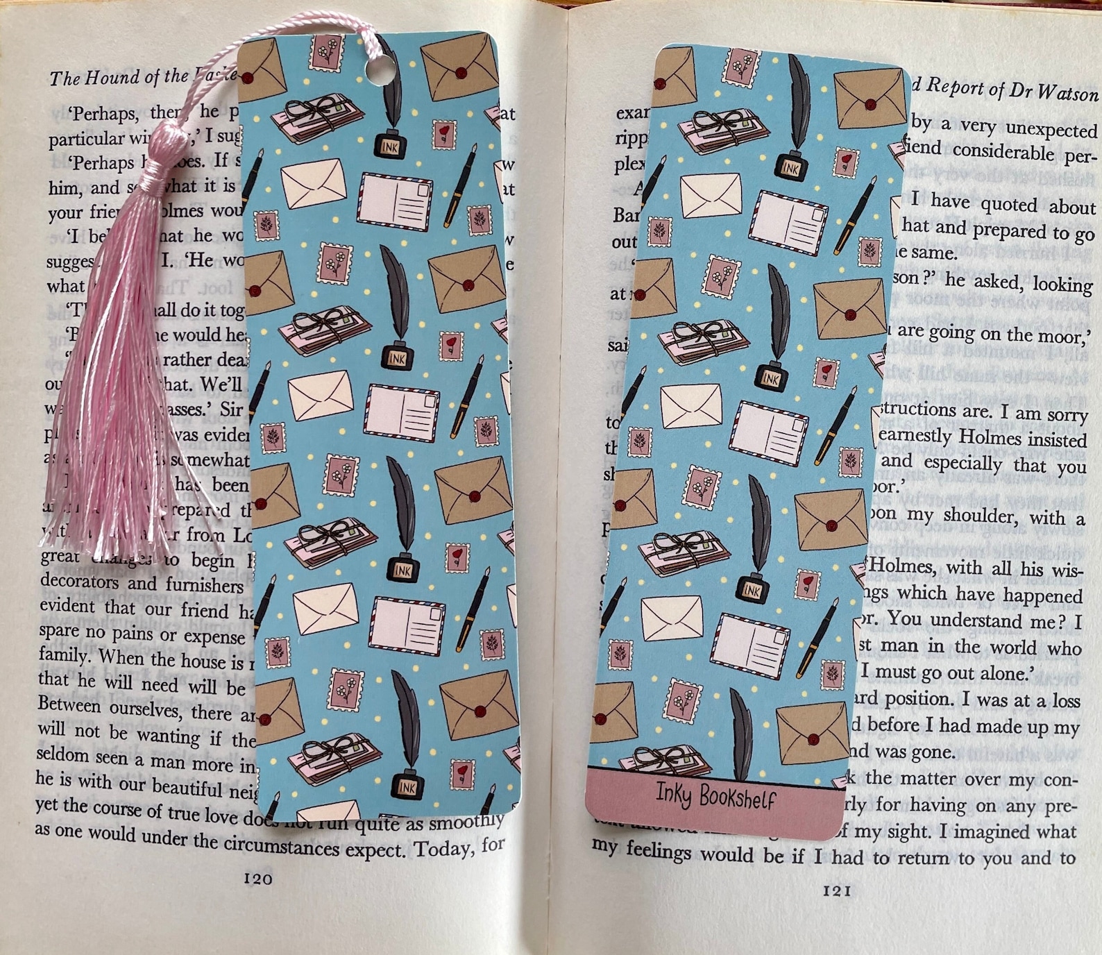 A blue bookmark on an open book with a pink tassel and hand drawn stationary illustrations.