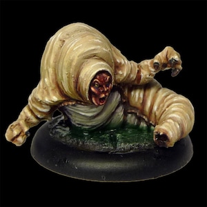 May include: A beige and white painted miniature figure of a creature with a human-like face and a body resembling a worm. The creature is posed in a crawling position with its arms outstretched.