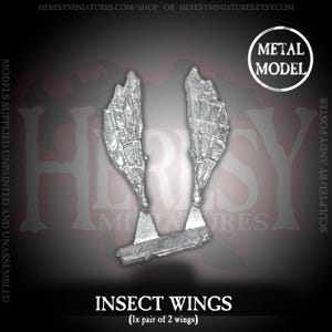 Puede incluir: Un par de alas de insecto de metal sin pintar, diseñadas para modelos en miniatura. Las alas tienen una superficie texturizada y detallada y están conectadas a una base rectangular. El texto "INSECT WINGS" y "METAL MODEL" está incluido.