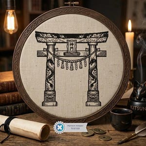 May include: A circular wooden embroidery hoop containing a beige fabric panel with a black cross-stitch design of a Japanese torii gate. The gate features intricate dragon carvings on the pillars, a shimenawa rope, and the kanji characters 神門.