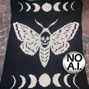 Può includere: Una coperta all'uncinetto bianca e nera con una grande falena centrale che presenta un motivo a teschio sul corpo. Il design include file di fasi lunari in alto e in basso. Il testo MOTH BLANKET è in alto e un badge circolare NO A.I. è a destra.