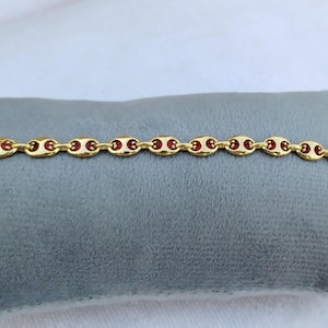 Puede incluir: Un brazalete de cadena dorada con detalles de esmalte rojo. El brazalete está hecho de pequeños eslabones ovalados.