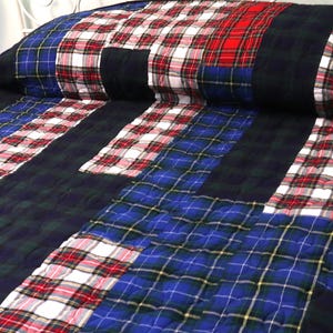May include: A quilted bedspread featuring a patchwork design of various tartan patterns in shades of blue, green, red, white, and black. The fabric squares are stitched together with a visible grid pattern across the entire surface of the textile.