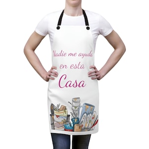 May include: White apron with a pink graphic that says "Nadie me ayuda en esta Casa" and a cartoon illustration of a pile of dirty dishes.