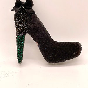 May include: A black high-heeled shoe with a green jeweled heel and a black bow on the top.