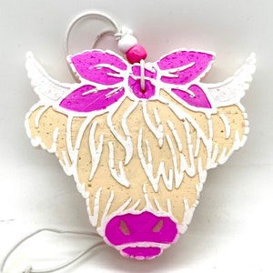 May include: A white and pink Highland cow ornament with a pink bow and white beads. The ornament is made of cork and has a white string for hanging.