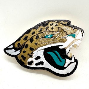 May include: A 3D printed jaguar head with a black outline, gold and brown spots, and teal accents. The jaguar's mouth is open and its teeth are visible.