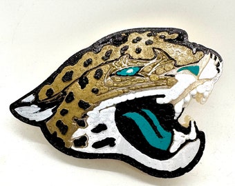 May include: A 3D printed jaguar head with a black outline, gold and brown spots, and teal accents. The jaguar's mouth is open and its teeth are visible.