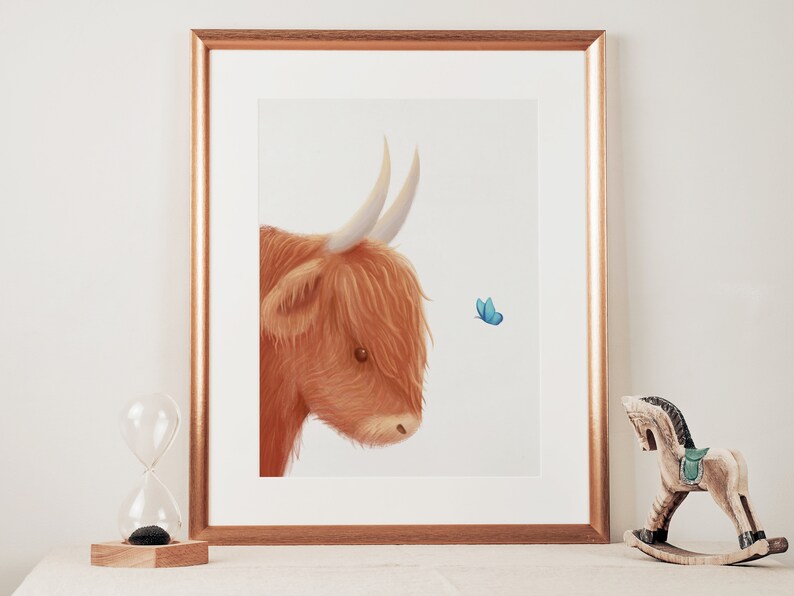 May include: A framed illustration of a Highland cow with a fluffy brown coat and large horns, looking to the right at a small blue butterfly.