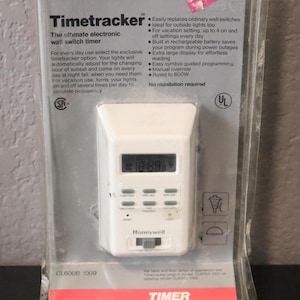 May include: A white Honeywell Timetracker electronic wall switch timer in its original clear plastic packaging. The device features a digital display, six rectangular buttons, a reset button, and a sliding switch at the bottom. Text on the packaging includes Honeywell, Timetracker, and technical specifications.