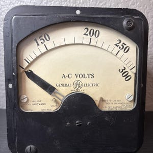 May include: Vintage General Electric A-C Volts meter. The black meter has a curved gauge with numbers from 150 to 300. The meter face is off-white with black text, including "A-C VOLTS" and "GENERAL ELECTRIC". Made in the U.S.A.