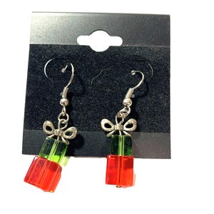May include: A pair of festive dangle earrings. Each earring features a red and green gift box design, topped with a silver bow. The earrings are suspended from silver-colored ear wires, perfect for holiday celebrations.