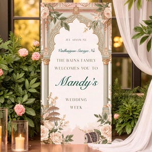 May include: A wedding welcome sign with floral and architectural design. The sign reads "Mandy's Wedding Week" and includes the names "The Bains Family". The sign is surrounded by greenery, candles, and a draped fabric.