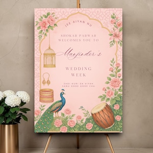 May include: A pink wedding sign with floral and peacock illustrations. The sign includes text that reads "Manjinder's Wedding Week". The sign is displayed on a gold easel.